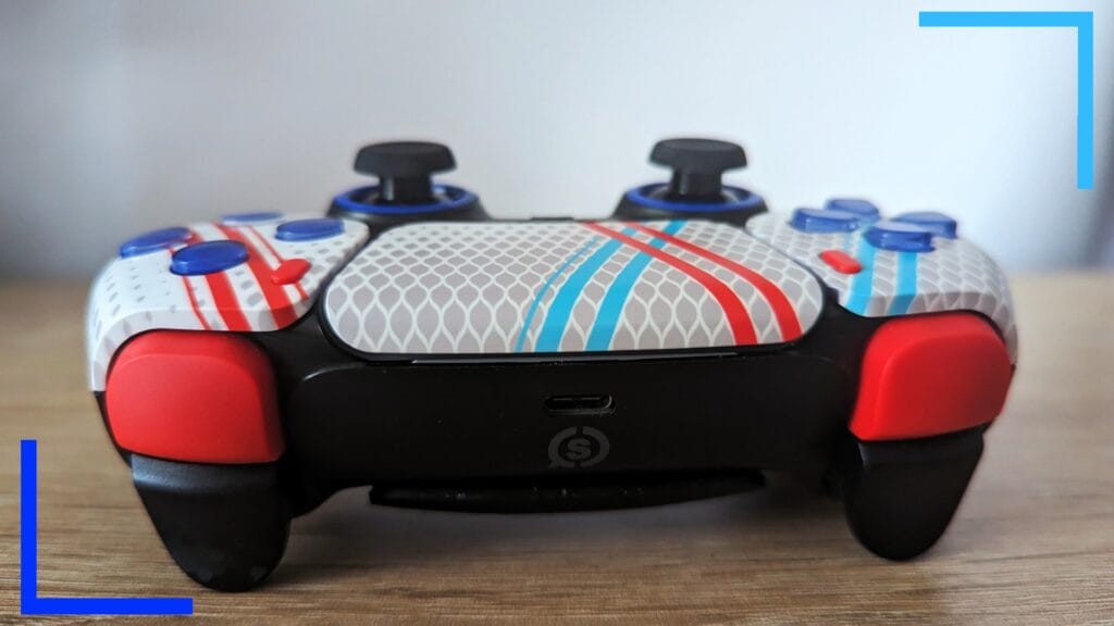 Фотография контроллера Scuf крупным планом сверху: красные бамперы, черные триггеры и белая с синими и красными полосами сенсорная панель.